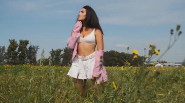 İnce, güzel esmer, kır çiçekleri ve mısır başakları arasında bir tarlada yürüyor.