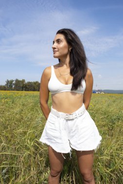 Güzel, narin esmer, kır çiçeklerinin arasında poz veriyor ve mısırın kulaklarında.