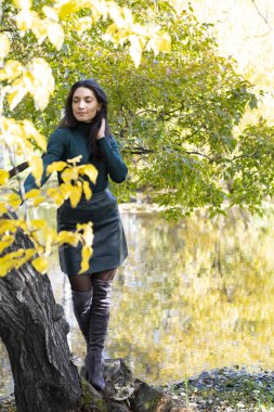 Kız, sonbahar manzarasının yansıdığı bir gölün kıyısında duruyor.