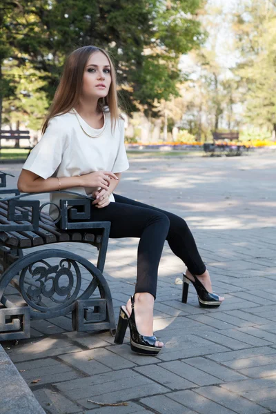 Chica joven sentada en un banco en el parque de otoño — Foto de Stock