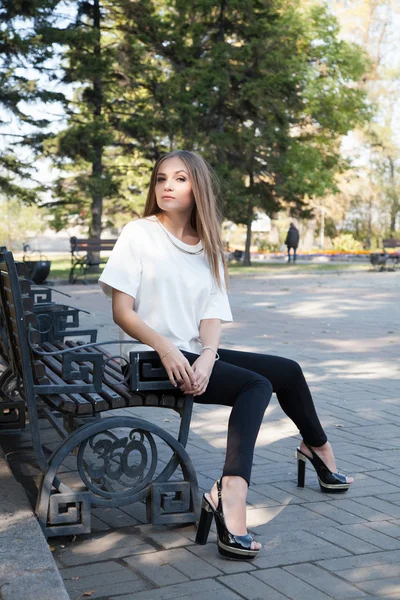 Jong meisje, zittend op een bankje in de herfst park — Stockfoto