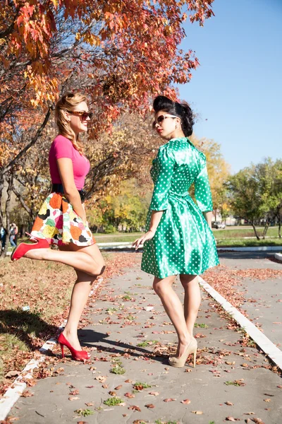 Two girls in colorful dresses walking in the autumn park — Stock Photo, Image