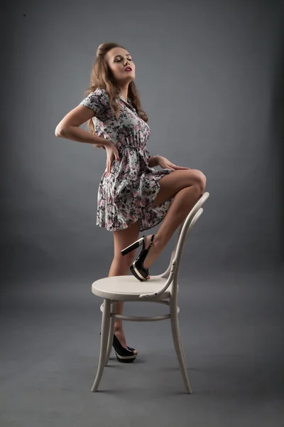 Studio portrait of a young girl in a short dress with a chair — Stock Photo, Image