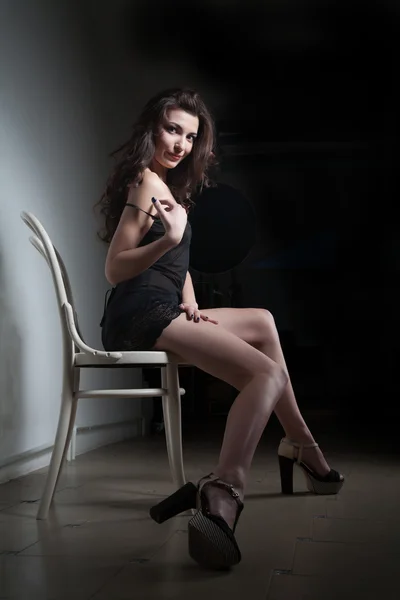 Fille assise sur une chaise dans une pièce sombre — Photo