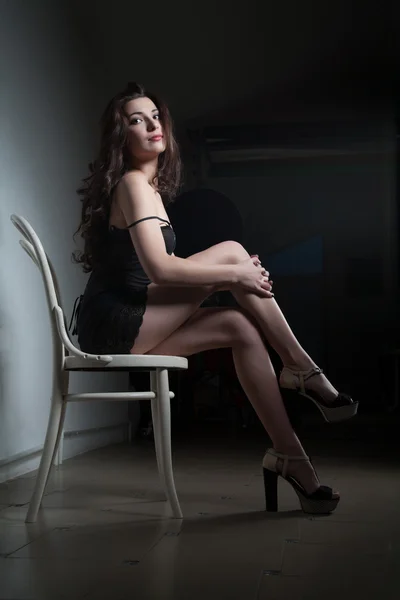 Meisje, zittend op een stoel in een donkere kamer — Stockfoto