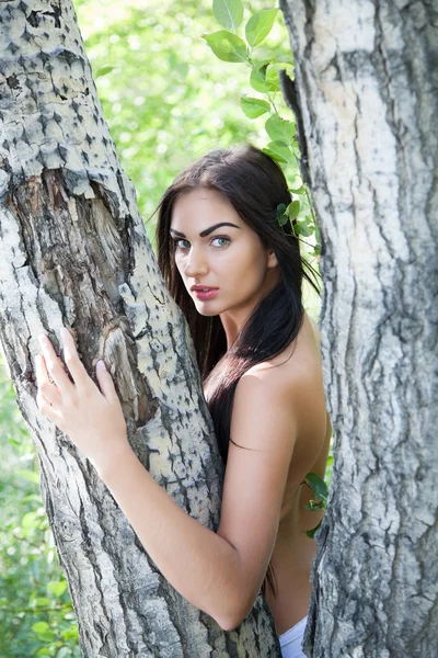 Chica con el pelo largo asomándose por detrás de un árbol — Foto de Stock