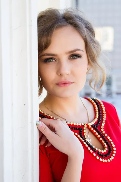 Meisje in een rode jurk permanent tegen de muur — Stockfoto