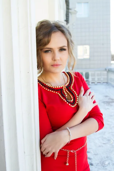 Girl in a red dress standing against the wall — Stock Photo, Image