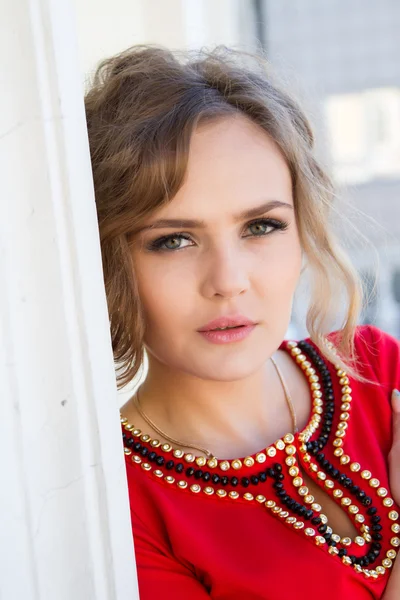Meisje in een rode jurk permanent tegen de muur — Stockfoto