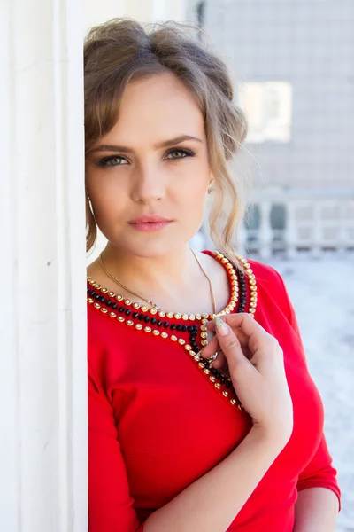 Girl in a red dress standing against the wall — Stock Photo, Image