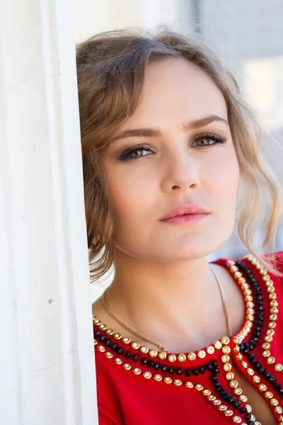 Girl in a red dress standing against the wall — Stock Photo, Image