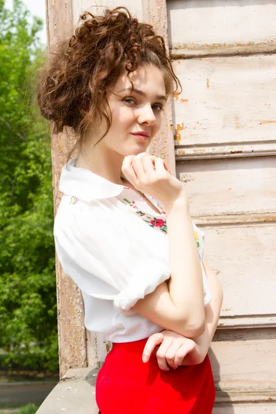 A girl in a white shirt embroidered on the front porch of an old wooden house — Stock Photo, Image