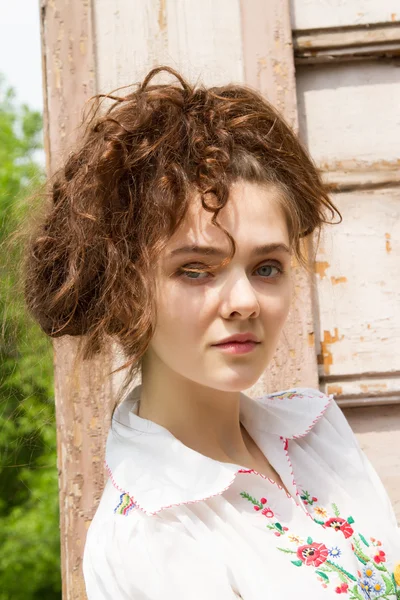 A girl in a white shirt embroidered on the front porch of an old wooden house — Stock Photo, Image