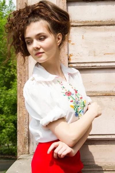 En flicka i en vit skjorta broderad på verandan i ett gammalt trähus — Stockfoto