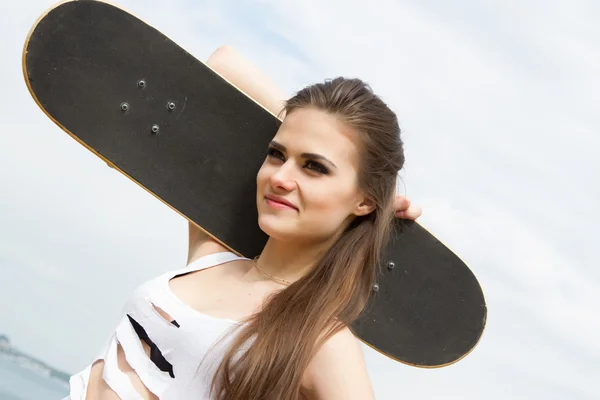 Sie trägt auf seiner Schulter ein Skateboard — Stockfoto