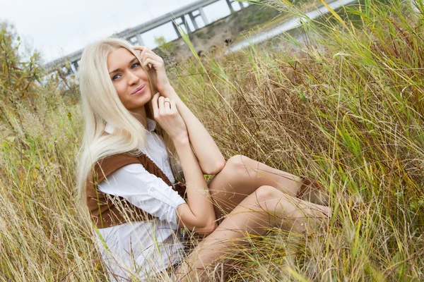 Блондинка сидит на берегу реки в траве — стоковое фото