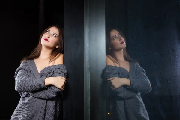 Mädchen steht am Fenster in einem dunklen Raum — Stockfoto