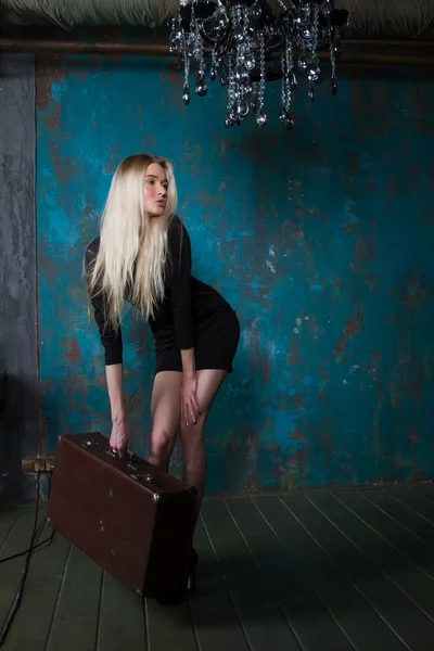 Blonde avec une valise dans une pièce sombre — Photo