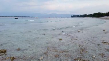 Sakin denizi ve bulutlu karanlık gökyüzüne karşı küçük dalgaları olan tropik Endonezya adası