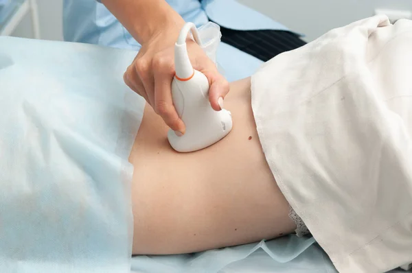 Bir doktor karın üstü yatan bir kadının ultrasonunu yapar. Ultrason araştırması