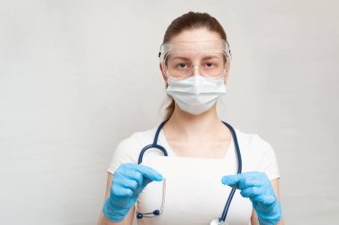 Maskeli, gözlüklü, eldivenli, steteskoplu kadın doktor elinde beyaz bir kağıt tutuyordu. Covid 19