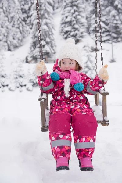 Liten flicka på snöig vinterdag swing i park — Stockfoto