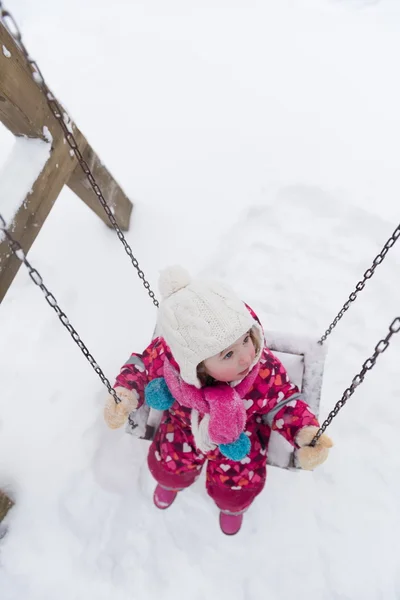 Liten flicka på snöig vinterdag swing i park — Stockfoto