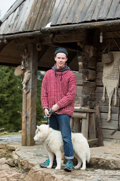 Joven hipster con perro delante de casa de madera —  Fotos de Stock