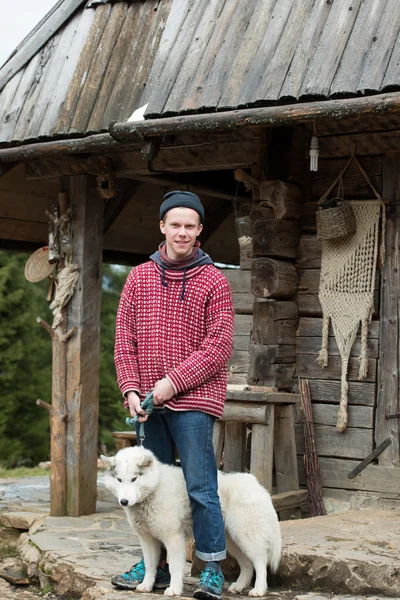 Joven hipster con perro delante de casa de madera — Foto de Stock