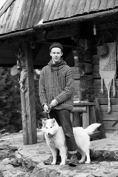 Joven hipster con perro delante de casa de madera — Foto de Stock