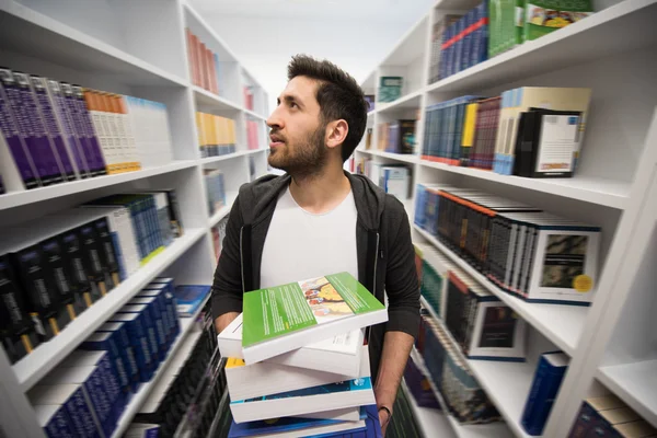 Estudante segurando muitos livros na biblioteca da escola — Fotografia de Stock