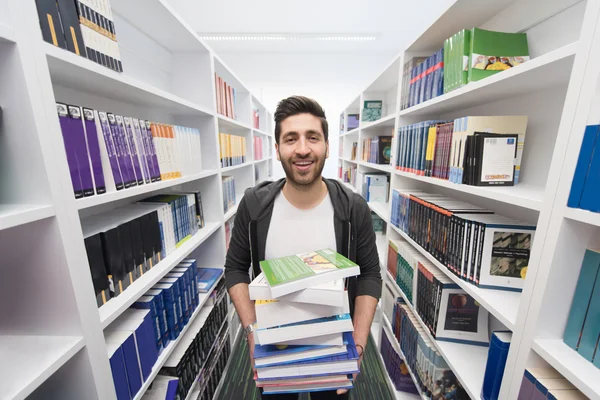 Estudante segurando muitos livros na biblioteca da escola — Fotografia de Stock