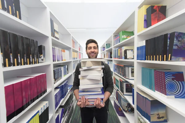 Estudante segurando muitos livros na biblioteca da escola — Fotografia de Stock