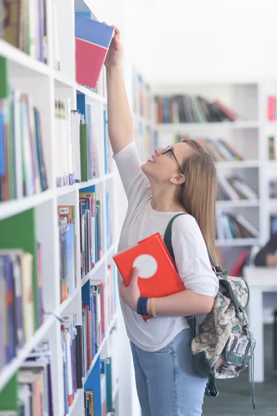 Estudante do sexo feminino selecionando livro para ler na biblioteca — Fotografia de Stock