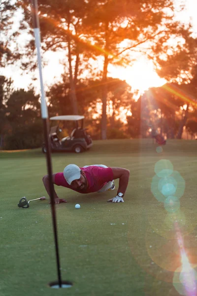 Golf player blowing ball in hole with sunset in background — Stock Photo, Image