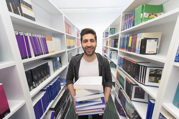 Estudiante sosteniendo muchos libros en la biblioteca de la escuela — Foto de Stock