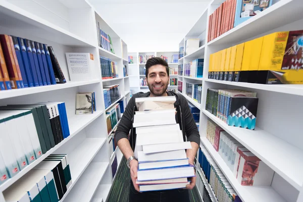 Estudante segurando muitos livros na biblioteca da escola — Fotografia de Stock