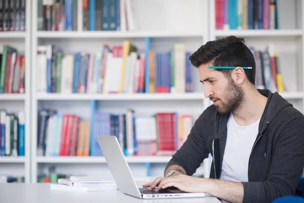 Estudiante en la biblioteca de la escuela usando el ordenador portátil para investigación —  Fotos de Stock