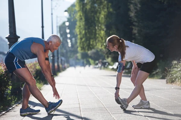 朝のランニング前にウォーミングアップやストレッチをしたり日の出を背景に街でトレーニングをしたり — ストック写真