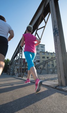 Sağlıklı olgun bir çift sabahın erken saatlerinde arka planda gündoğumuyla birlikte şehirde koşuyor.