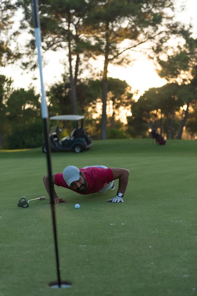 Jogador de golfe soprando bola no buraco com o pôr do sol no fundo — Fotografia de Stock