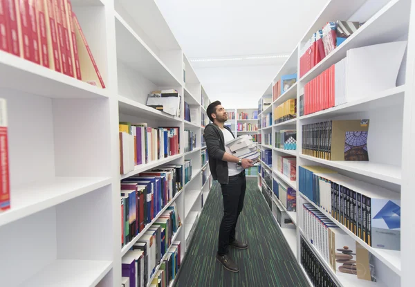 Student trzymający wiele książek w bibliotece szkolnej — Zdjęcie stockowe