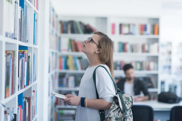 Famale studente selezionando libro da leggere in biblioteca Foto Stock Royalty Free