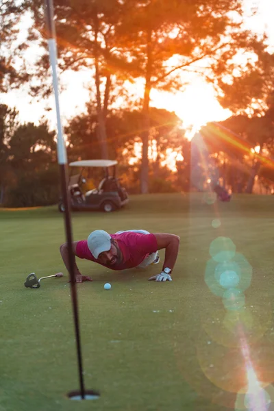 Jogador de golfe soprando bola no buraco com o pôr do sol no fundo — Fotografia de Stock