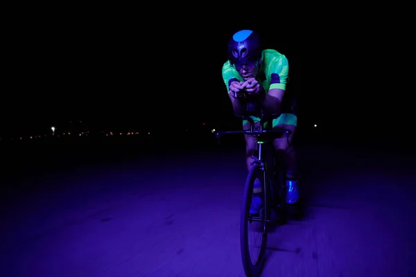 triathlon athlete cycling fast riding professional racing bike at night neon color gel lights