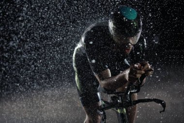 Yağmurlu bir gecede bisiklet süren triatlon sporcusu
