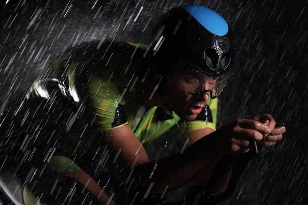 Triathlon athlete riding bike fast on rainy night — Stock Photo, Image
