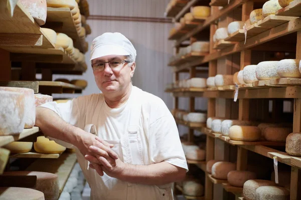 Cheese maker at the storage with shelves full of cow and goat cheese — Stock Photo, Image