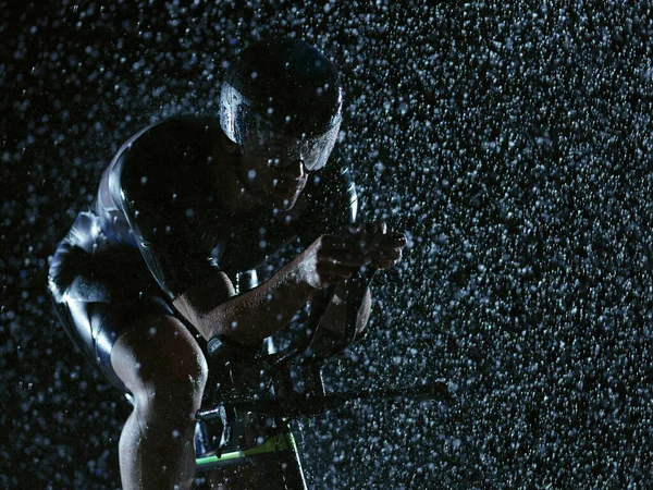 Triathlon athlete riding bike on rainy night — Stock Photo, Image