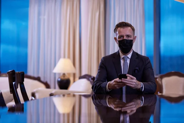 Uomo d'affari utilizzando smart phone in ufficio di lusso indossando maschera — Foto Stock